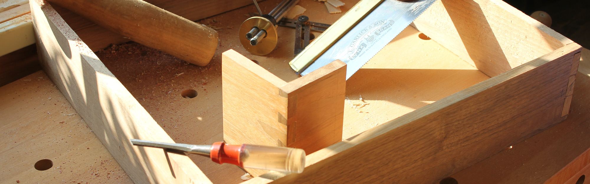 A dovetailed drawer box on the bench beside a dovetail saw, chisel, mallet and marking gauge