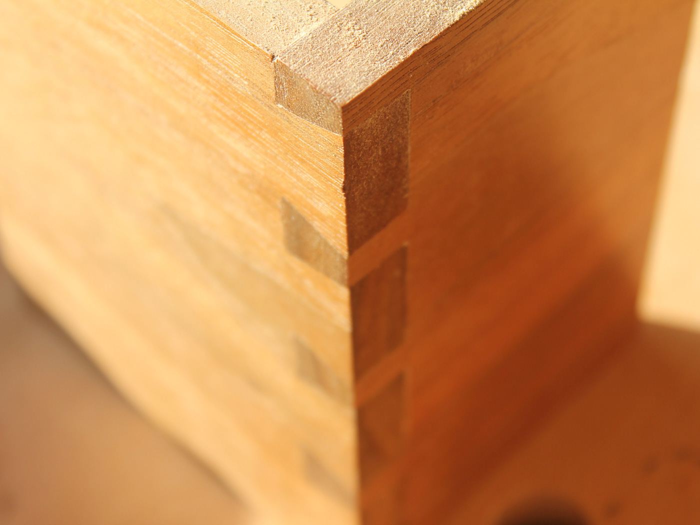 A close-up of a hand-cut dovetail joint at the corner of a drawer box