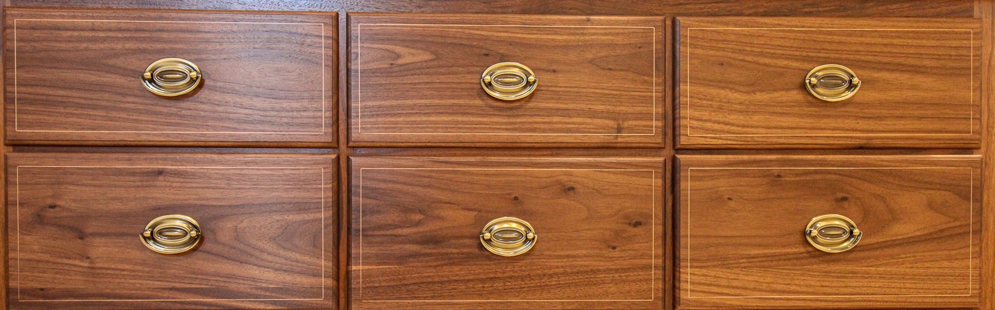 Walnut drawer fronts with fine string inlay and oval brass pulls on a finished chest